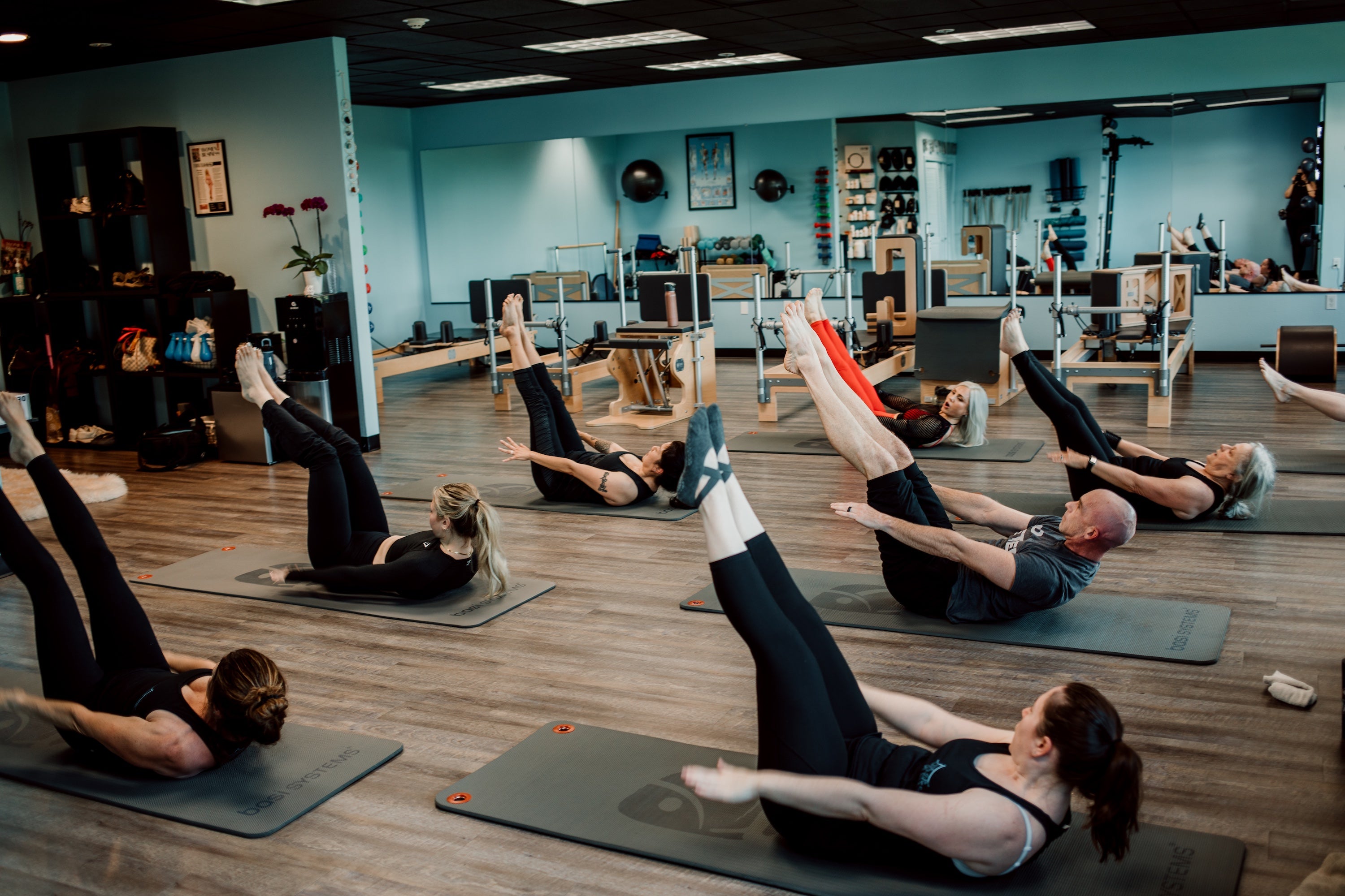 Group of people exercising on mats in a fitness studio with blue walls and wooden floors.